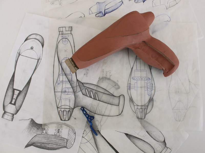 Clay model of an instrument handle beside design sketches